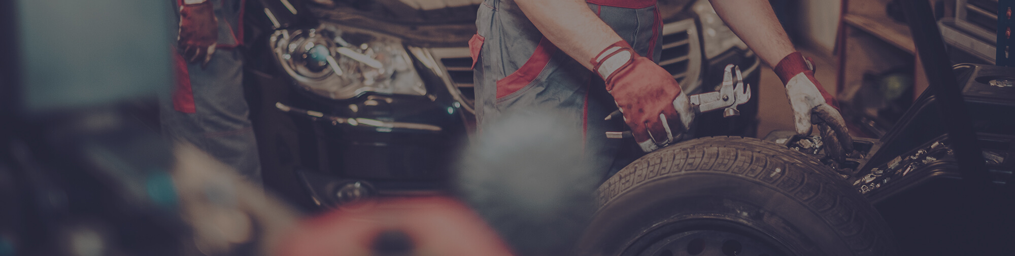 Mechanic holding a wrench and looking under the hood of a car